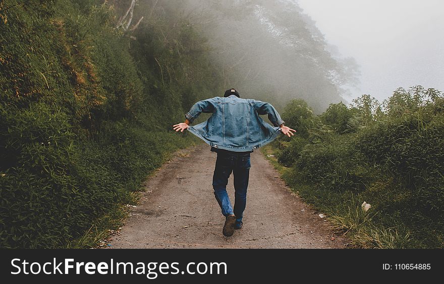 Person Wearing Blue Denim Jacket While Walking on Foggy Road