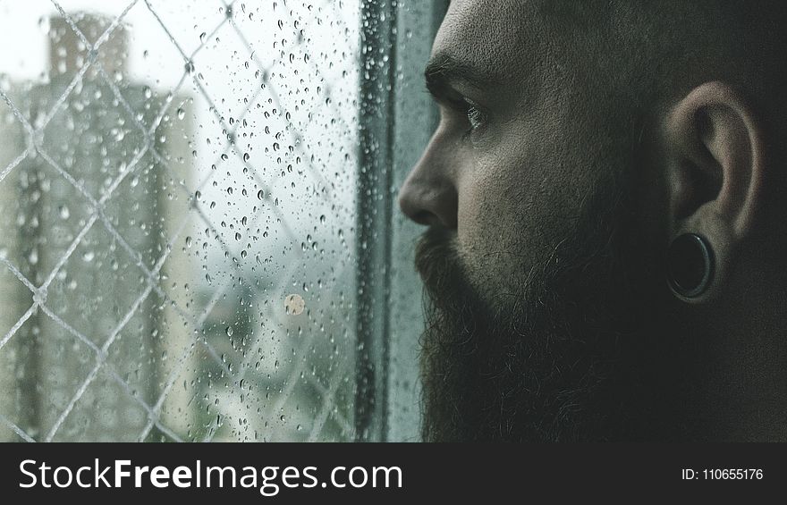 Selective Focus Photography of Man Staring on Glass Window Filled With Droplets