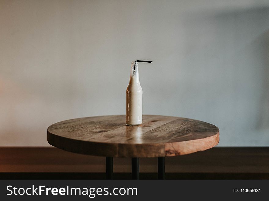 Glass Bottle Filled With Black Straw on Brown Wooden Table