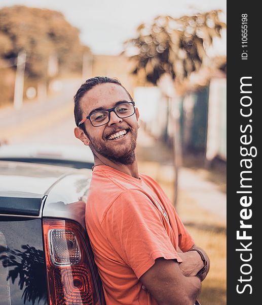 Man in Orange T-shirt Leaning on a Car