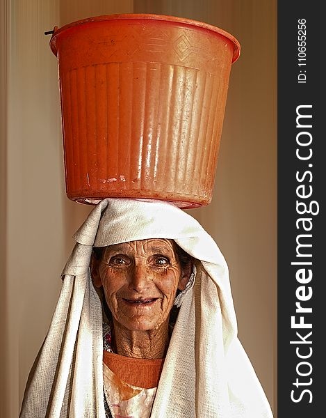 Portrait Photo of Woman Carrying Orange Plastic Pail on Head