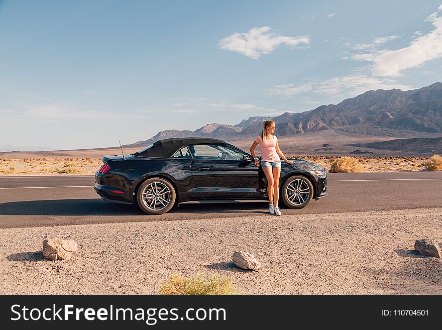 Young girl standing by the black Ford Mustang GT convertible at the side of the road. Nevada, USA.
