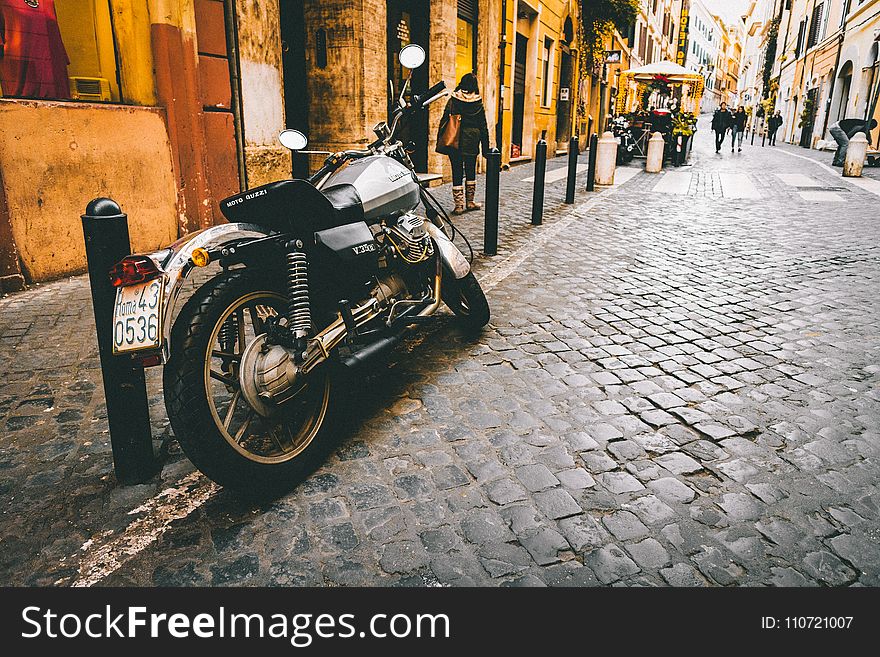 Photograph of Motorcycle Parked Beside Park Bars Near Woman Walking Through Street