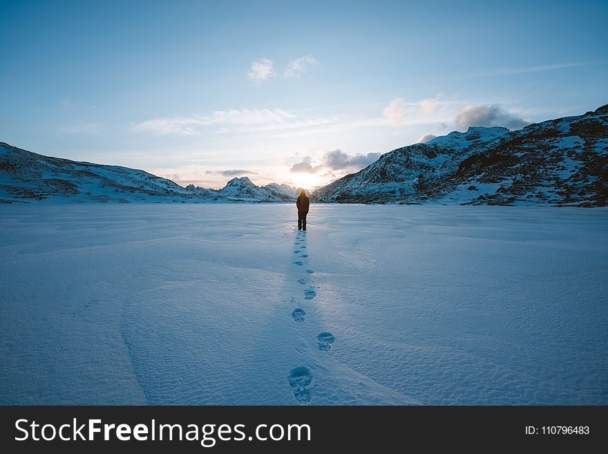 Person Walking In Snow Field Near Mountain Cliff Covered With Snow