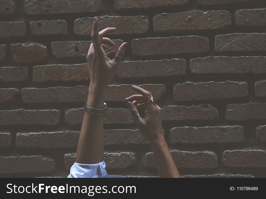 Person Raising Its Two Hand Beside Brown Brick Wall