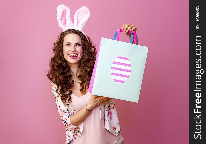 Festive bunny and eggs season. happy modern woman in Easter bunny ears isolated on pink background with Easter shopping bag looking at copy space. Festive bunny and eggs season. happy modern woman in Easter bunny ears isolated on pink background with Easter shopping bag looking at copy space