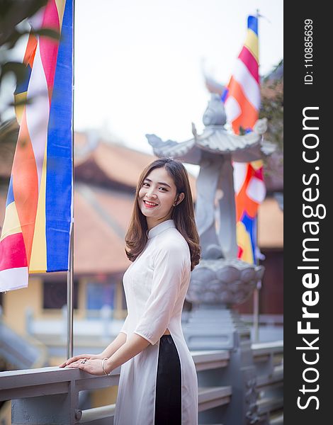 Depth of Field Photo of Woman Wearing White Dress Standing Near Flag Pole