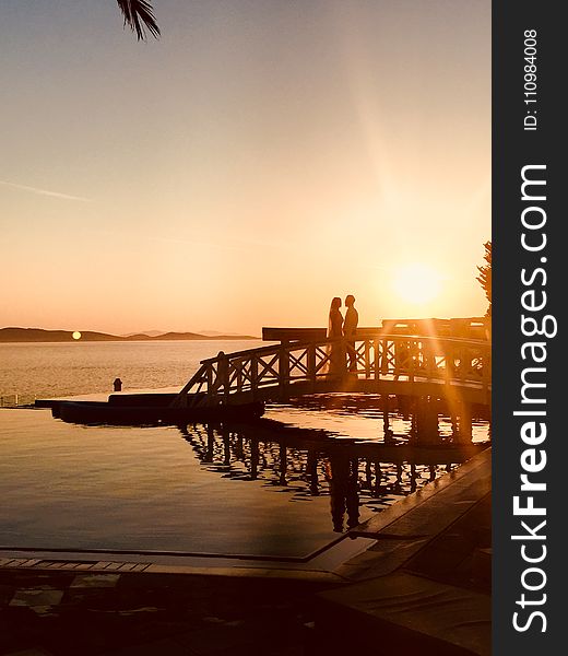 Silhouette of Couple Standing Near Sea Dock at Golden Hour