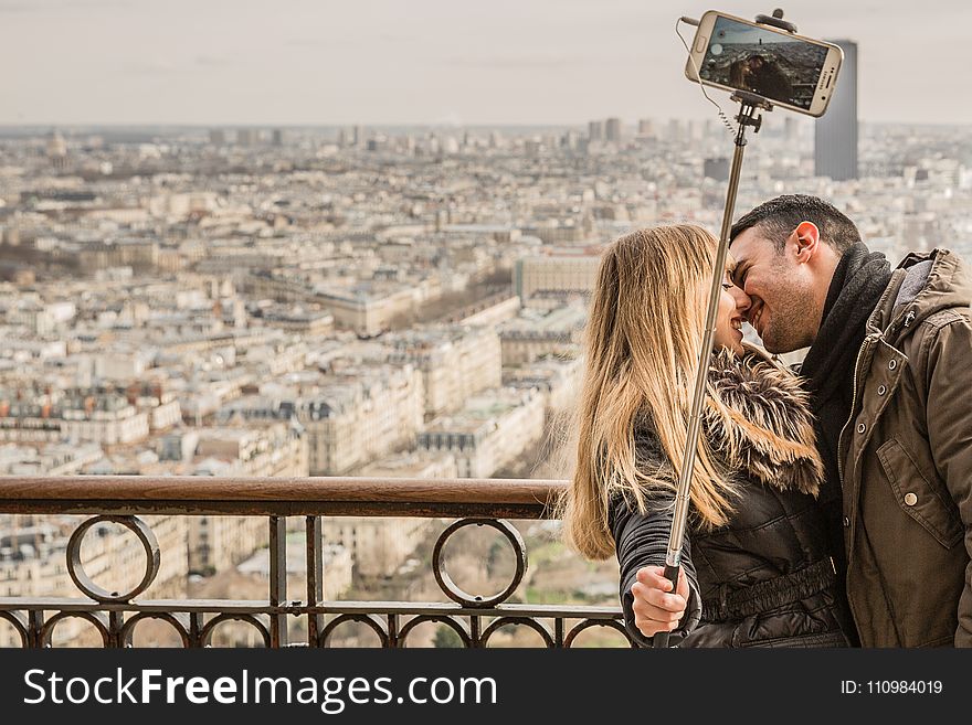 Man Kissing Woman Holding Selfie Stick