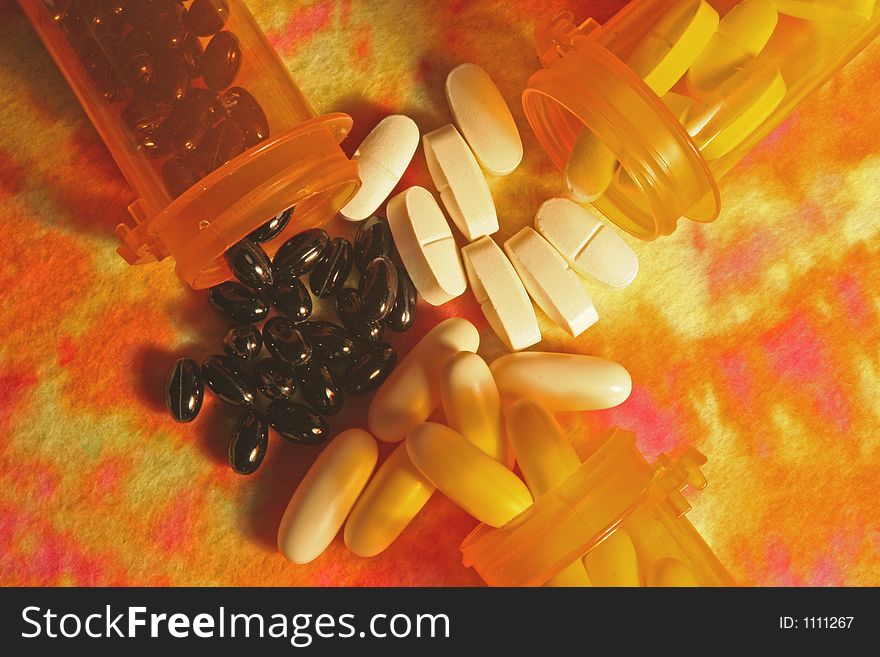 Horizontal image of three prescription bottles filled with pills spilling out on multi-colored background. Horizontal image of three prescription bottles filled with pills spilling out on multi-colored background