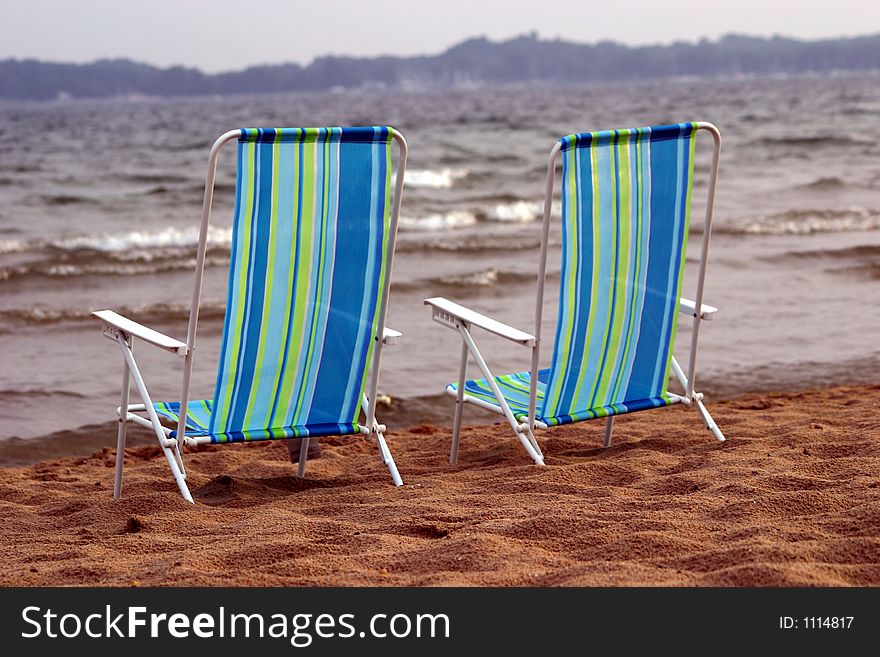 A pair of beach chairs sit side by side on the beach empty