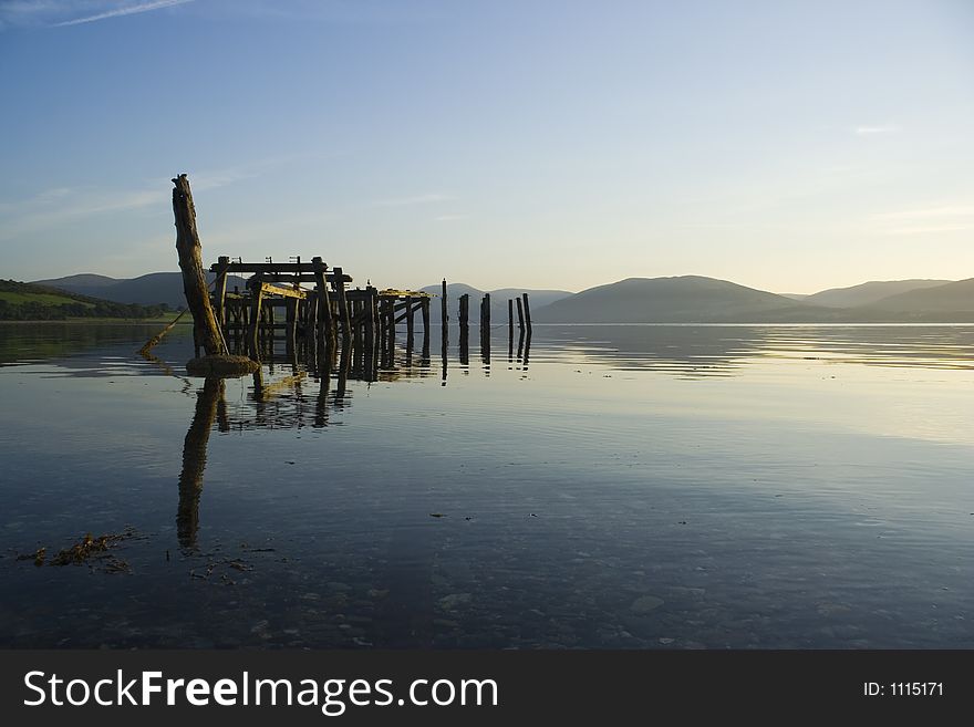 A ruined pier reflected in the calm of a morning seashore at Port Bannatyne, Bute, Scotland