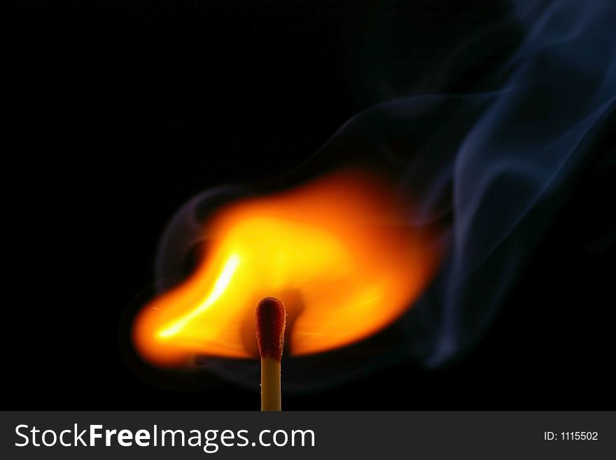 Closeup of a red-tipped wooden match stick at ignition with visible smoke.  Red, orange, yellow, and white flame.  Black background. Closeup of a red-tipped wooden match stick at ignition with visible smoke.  Red, orange, yellow, and white flame.  Black background.