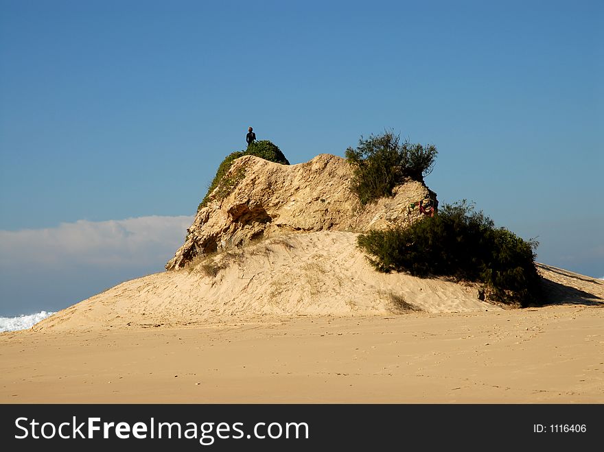 Man Standing On A Rocky Sand Dune Looking Out To Sea