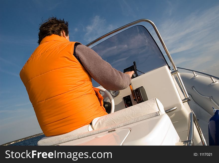 Captain at the steering wheel of a modern speedboat with coastline in the background. Captain at the steering wheel of a modern speedboat with coastline in the background.