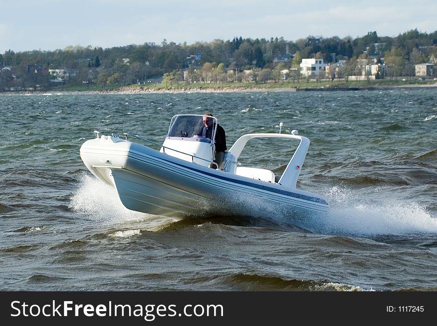 Modern lightweight speedboat speeding in the sea with the coastline visible nearby in the background. Modern lightweight speedboat speeding in the sea with the coastline visible nearby in the background.