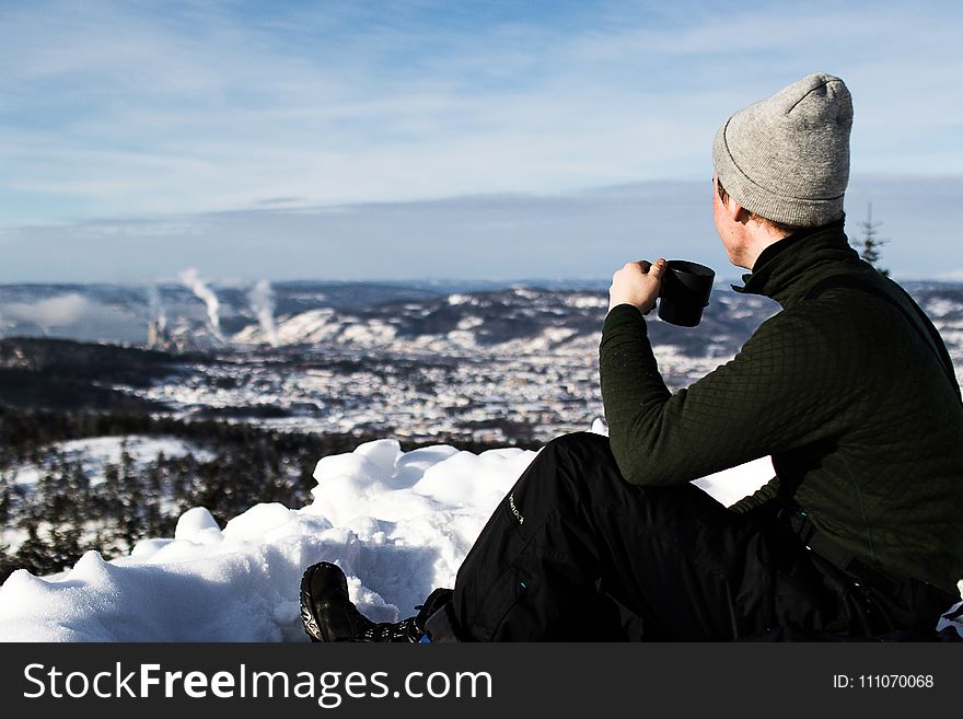 Man Wearing Jacket And Holding Cup Sitting On The Snow