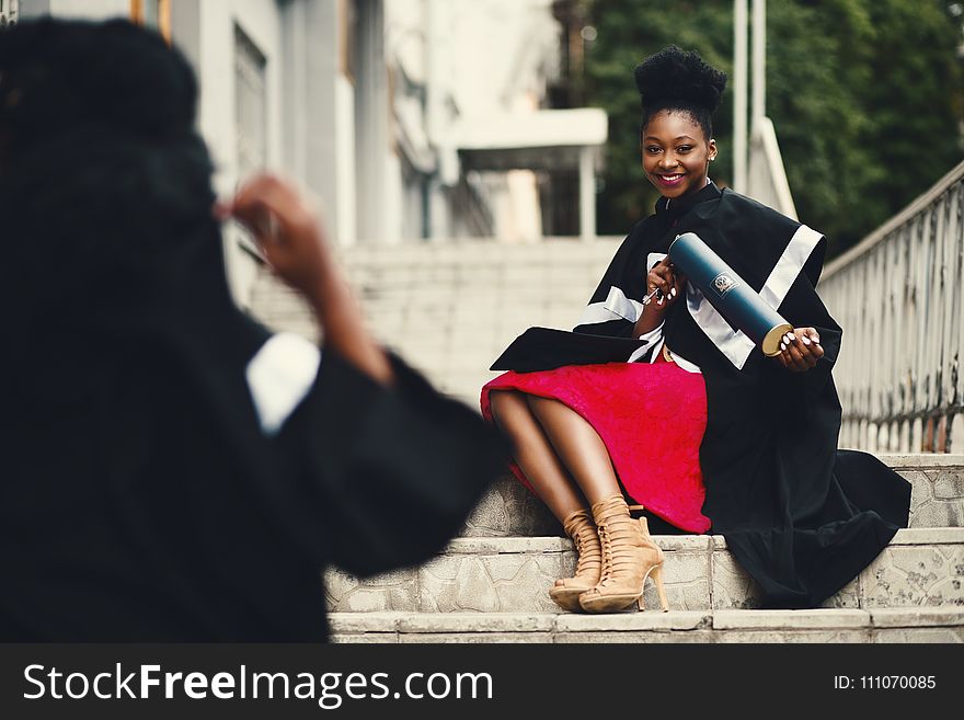 Woman Wearing Black Graduation Coat Sits On Stairs