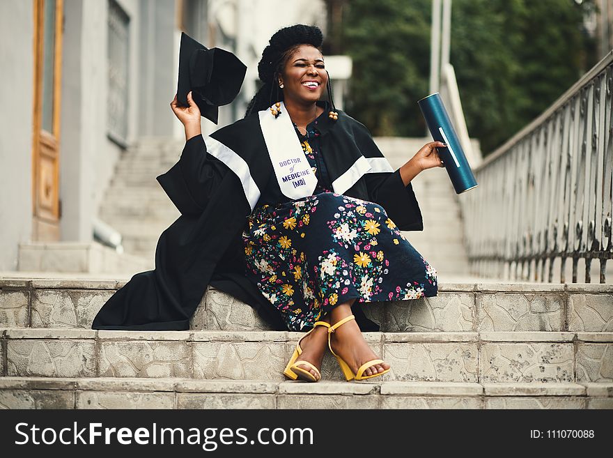 Photo of Woman Wearing Academic Dress and Floral Dress Sitting on Stairway