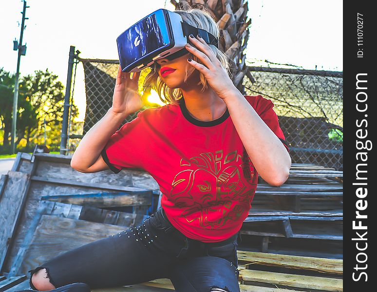 Woman Wearing Red and Black Top and Blue Distressed Bottoms Wearing Gray and Black Virtual Reality Sunglasses