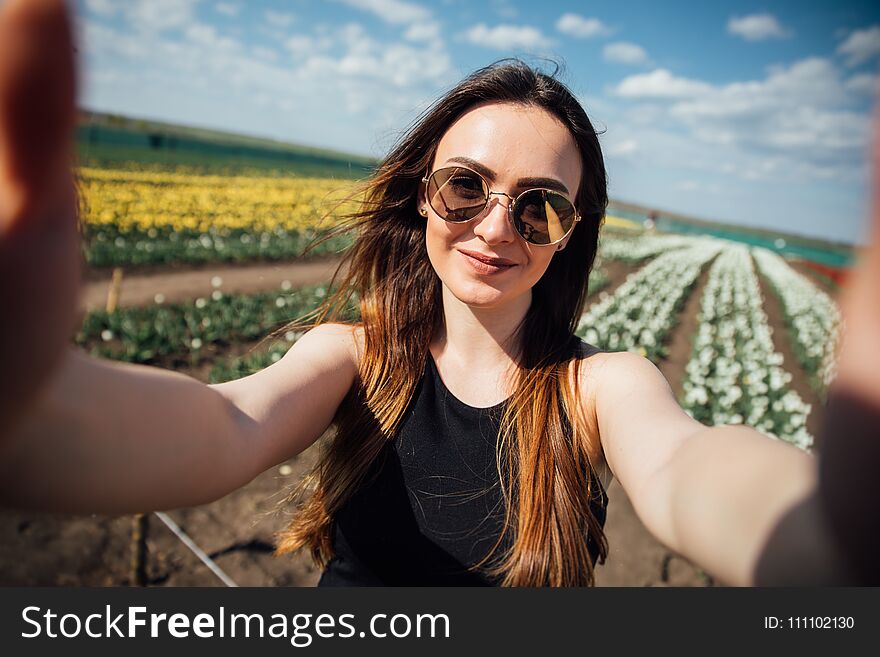 Young beautiful woman wear sunglasses make selfie in tulips flower field in sunny spring day