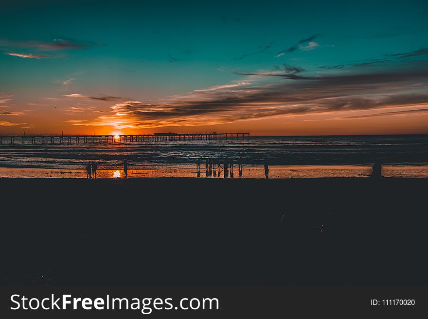 Silhouette Of People Near Body Of Water At Golden Hour