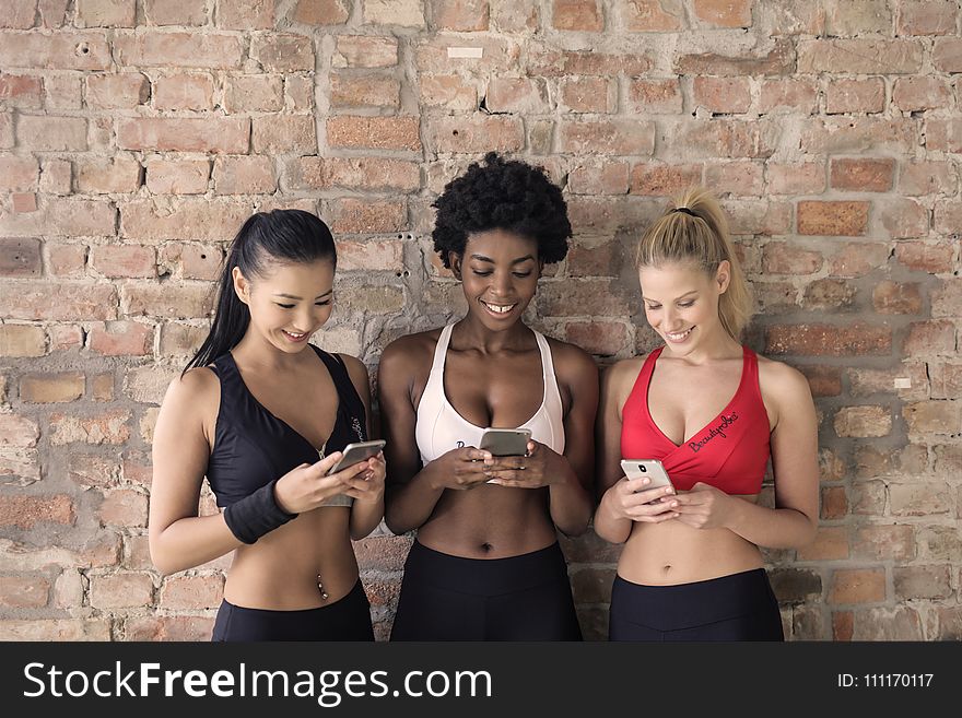 Three Woman in Assorted-color Sport Bras Holding and Watching Their Smartphones
