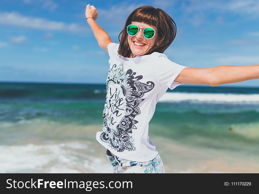 Woman In White And Black T-shirt Lifting Hands Smiling On Seashore