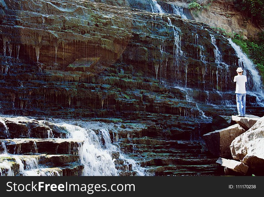 Man in White T-shirt and Blue Jeans Standing Near Water Falls