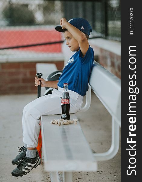 Selective Focus Photo Of A Boy Wearing Baseball Gear Sitting On Bench Beside Coca-cola Bottle