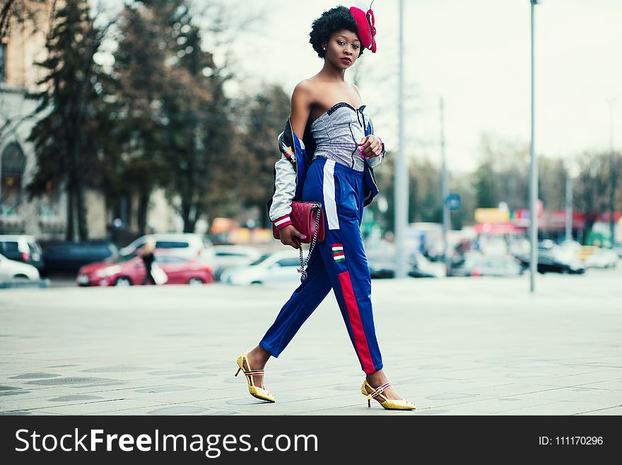 Woman Wearing White Sweetheart Neckline Shirt With Blue and Red Pants Walking Across the Street