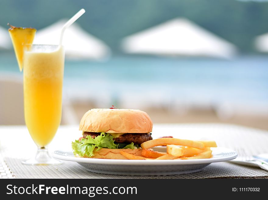 Burger With Lettuce and Fries on Plate Beside Pineapple Juice