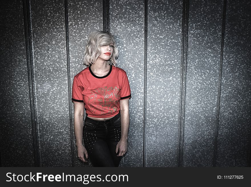 Woman Wearing Red and Black Scoop-neck Shirt and Black Bottoms Leaning on Gray Wall
