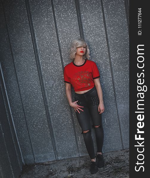 Woman Wearing Red Shirt Leaning on Gray Wall