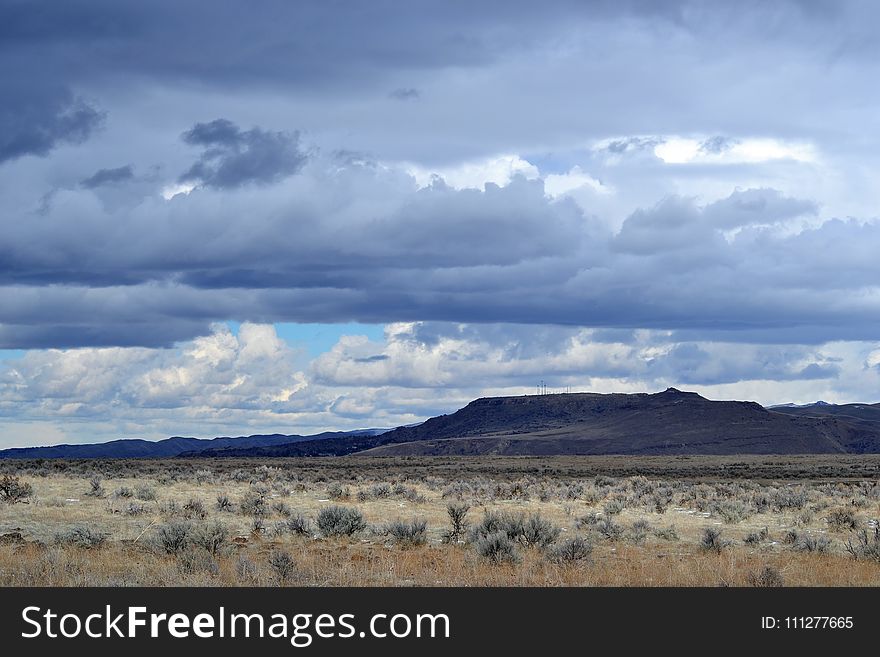 Gray Grass Field Leading to Mountains Under Gray Heavy Clouds