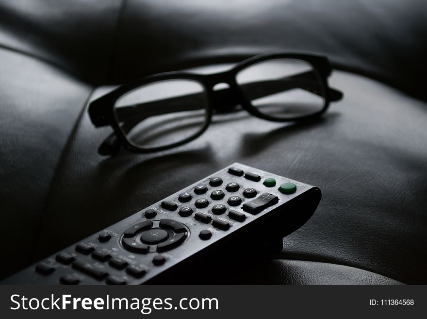 Grayscale Photo of Remote Control Near Eyeglasses