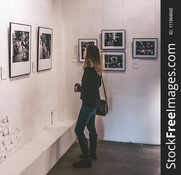 Woman Wearing Black Sweater and Blue Denim Jeans Staring at Paintings Inside Well-lit Room