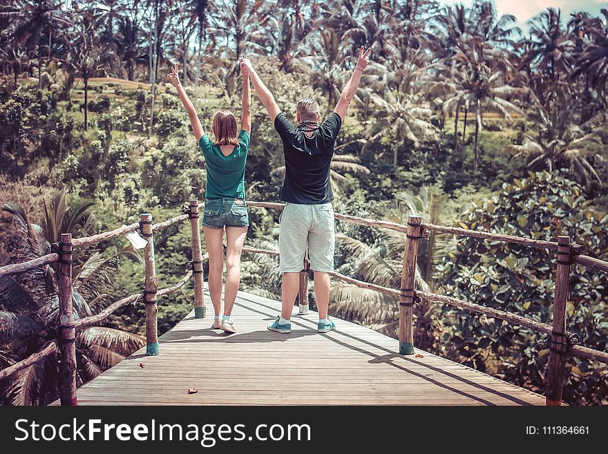 Man Wearing Black Shirt Beside a Woman in Green Shirt Raising Their Hands in the Air