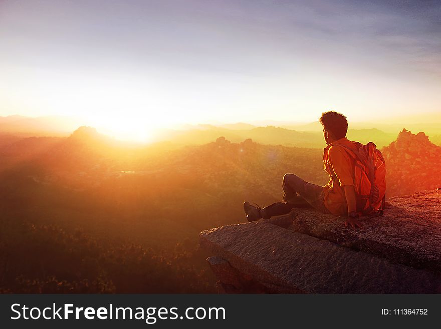 Man Sitting On Edge Facing Sunset