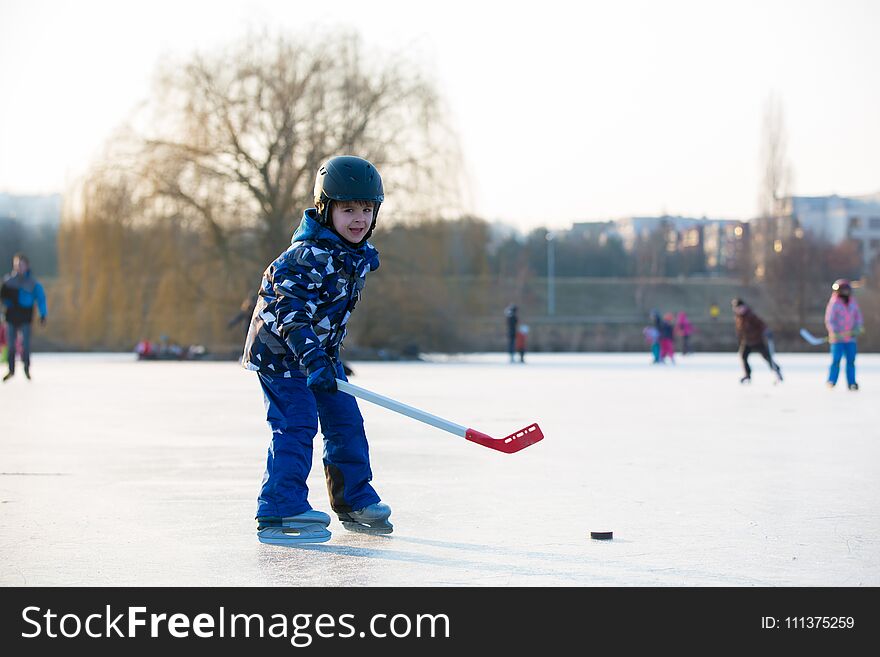 Children, boys, friends and brothers playing hockey and skating in the park on frozen lake, wintertime on sunset. Children, boys, friends and brothers playing hockey and skating in the park on frozen lake, wintertime on sunset