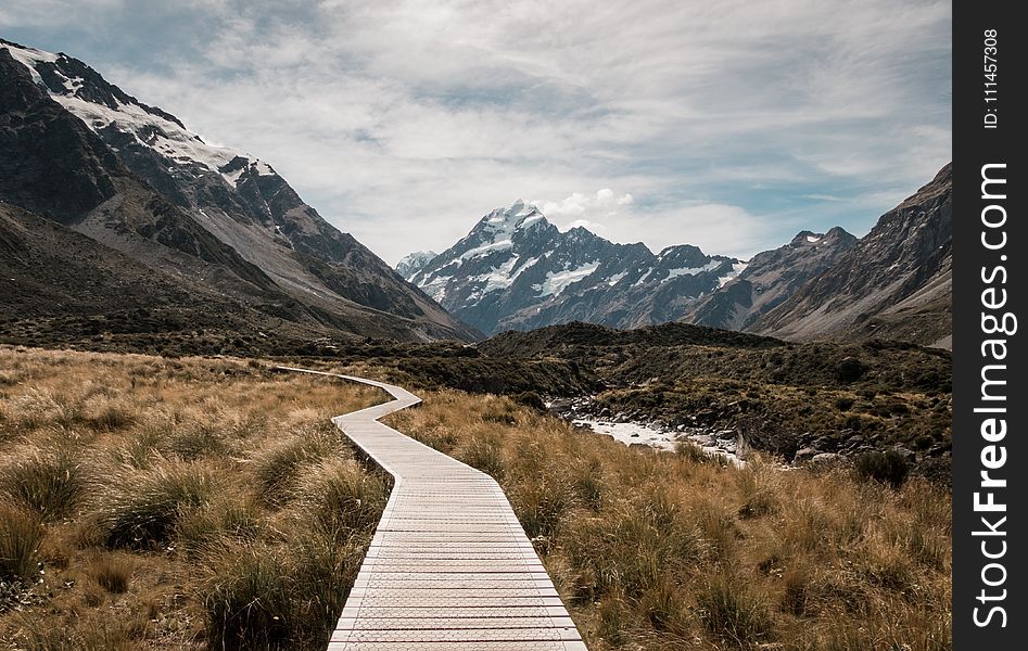 Brown Wooden Dock Surrounded With Green Grass Near Mountain Under White Clouds and Blue Sky at Daytime