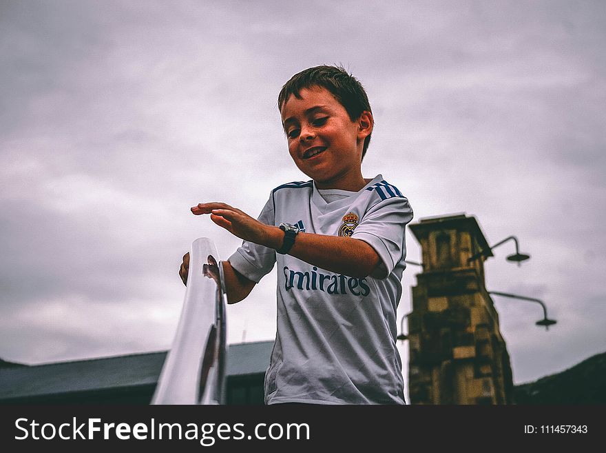 Boy in White and Blue Fly Emirates Jersey Shirt Holding on Stairs Grab Bar Under Gray Skies