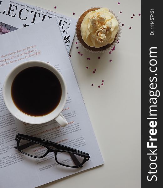 White Ceramic Cup With Coffee on Top of Opened Book and Near Eyeglasses