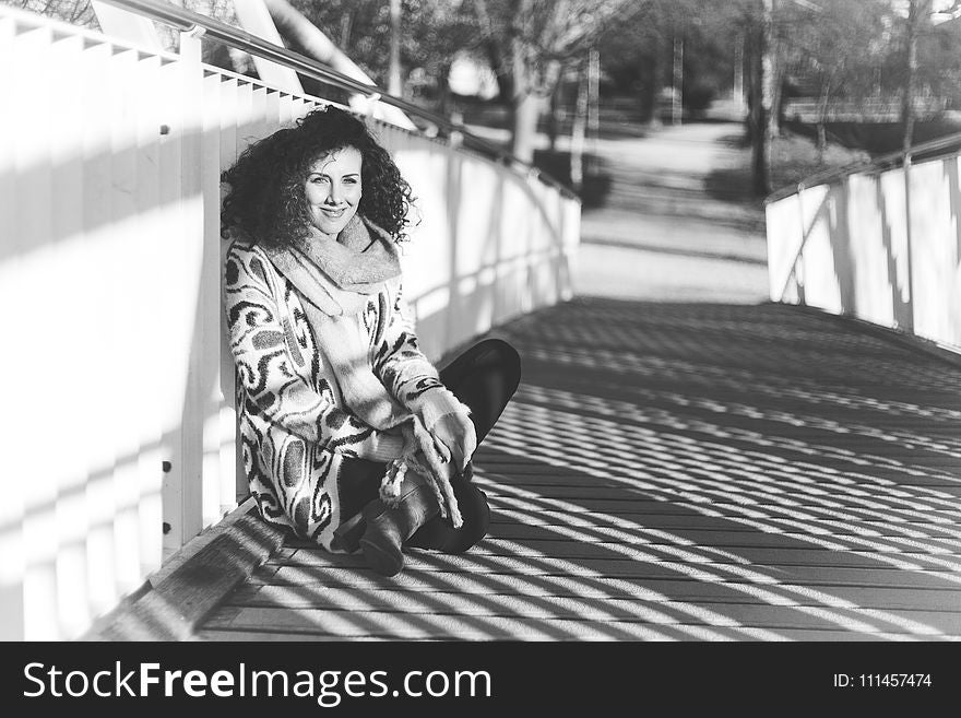 Grayscale Photography of Woman Sitting on Bridge
