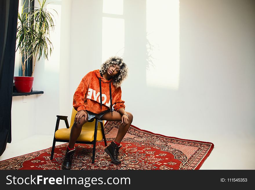 Woman Wearing Orange Pullover Hoodie Sitting on Chair&#x27;s Arm