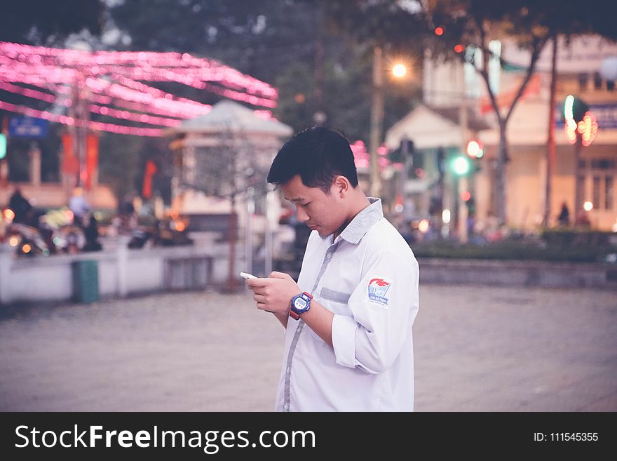 Focus Photography of Man Wearing White Sports Shirt Holding Smartphone Near Buntings