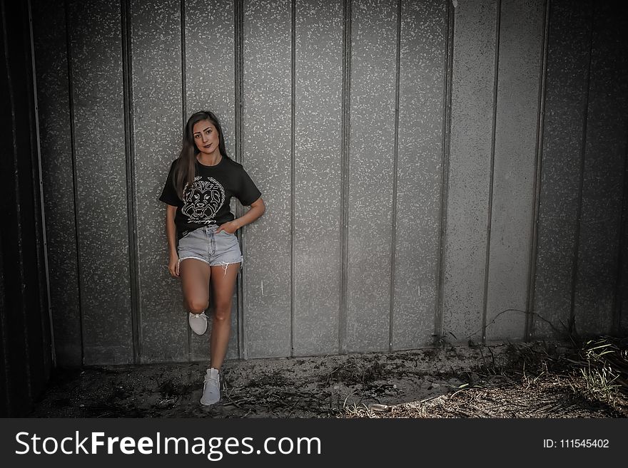 Woman Wearing Black Shirt and Daisy Dukes Leaning on Wall