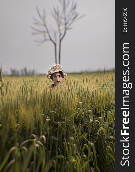 Toddler Wearing Brown Hat in the Middle of Green Field
