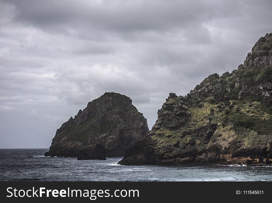 Brown Rock Formation On Body Of Water Under Gray Clouds