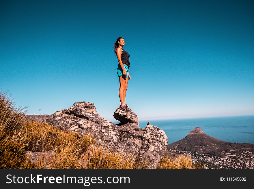 Woman in Black Top and Blue Shorts on Stone Under Blue Sky
